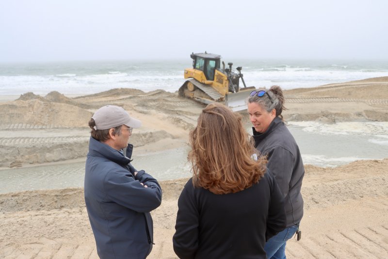 A bulldozer moves sand on the north side of the Indian River Inlet, as DNREC Secretary Greg Patterson, left, and Kathleen Bergin, field operation program manager, explain how the sand bypass works to Congresswoman Sarah McBride.
